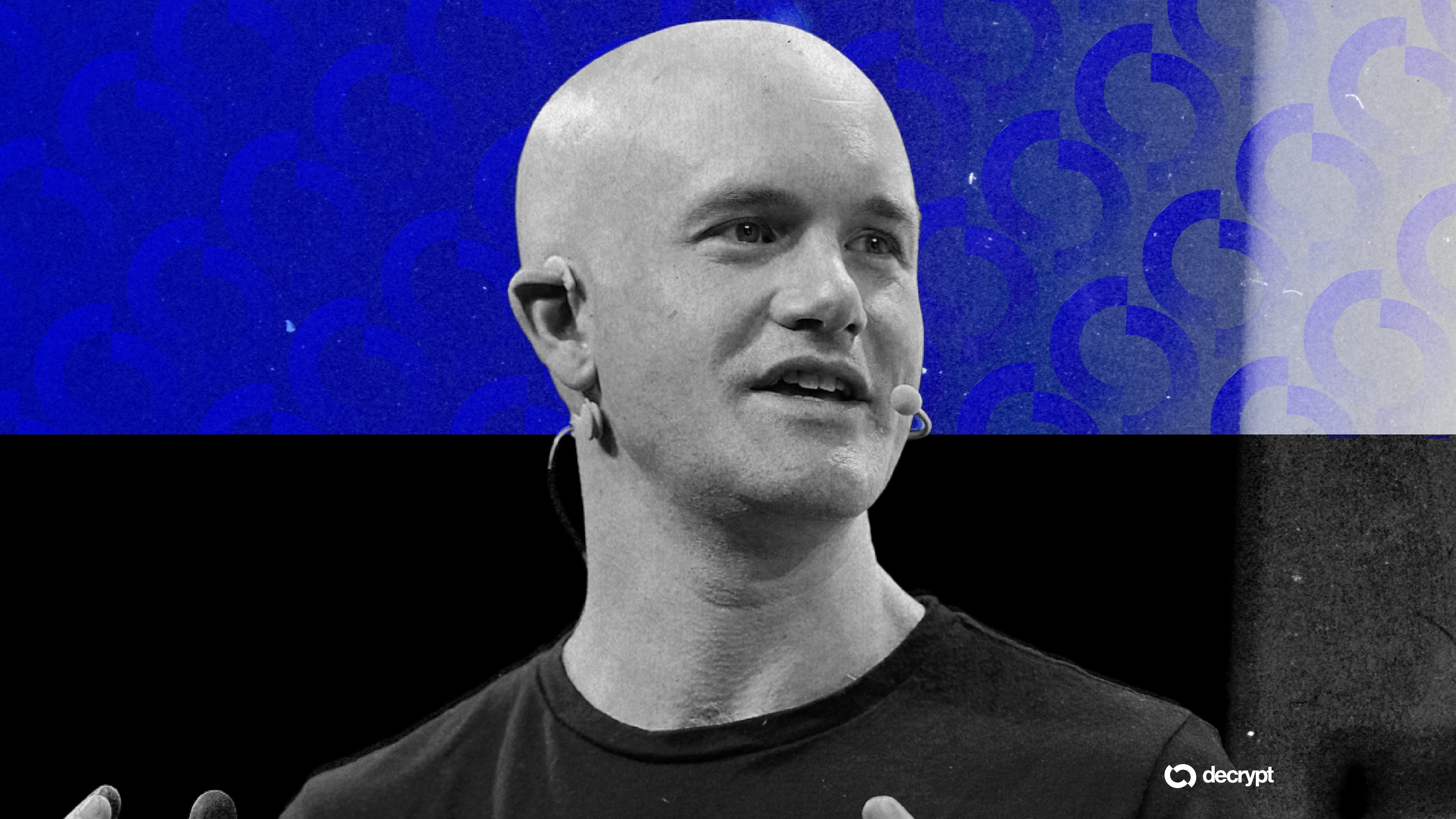 Bald man wearing a black t-shirt and headset microphone speaks on stage against a blue patterned backdrop.