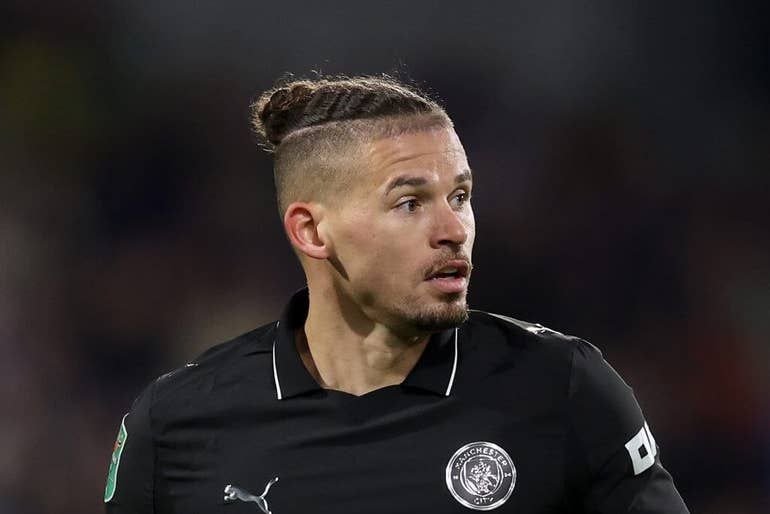 A male footballer with a man bun hairstyle, wearing a black Puma jersey with a "Sackeey City" club crest, looks off to the side during a match.