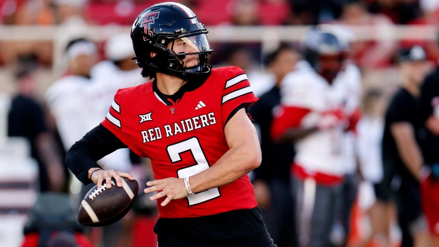 A football player in a red "Red Raiders" jersey (#2) and black helmet holds a football while looking to pass during a game.