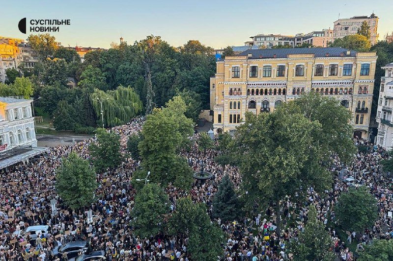 A large crowd gathers in a tree-lined city street beside an ornate yellow building, with the "Суспільні Новини" logo visible in the corner.