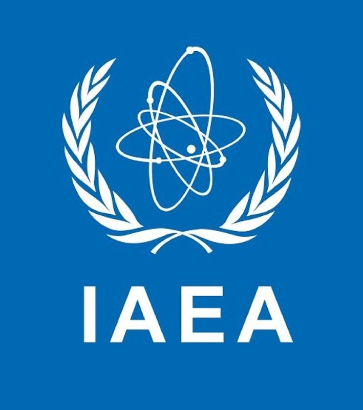 A blue logo featuring a white atomic symbol encircled by laurel branches above the letters "IAEA."