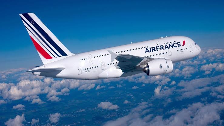 An Air France double-decker aircraft, marked F-HP-JA, flies above white clouds in a clear blue sky.