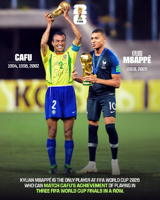 Soccer players in blue jerseys celebrate together on a stadium pitch while opposing players in white and an orange-uniformed goalkeeper stand nearby before a packed crowd.