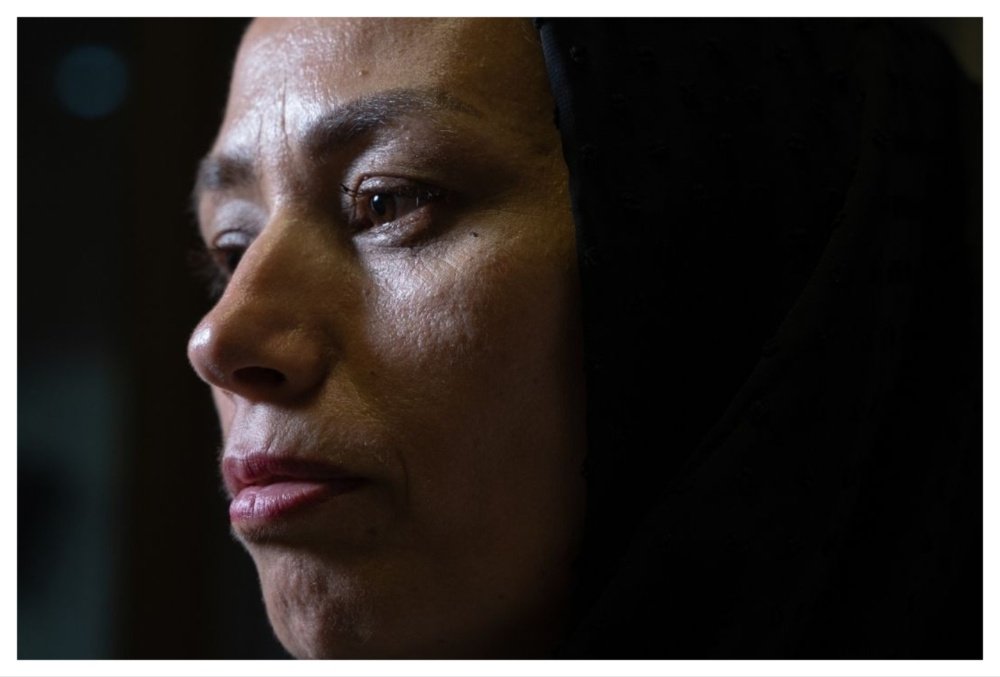 Close-up profile of a woman wearing a black head covering, gazing forward with a serious expression against a dark background.