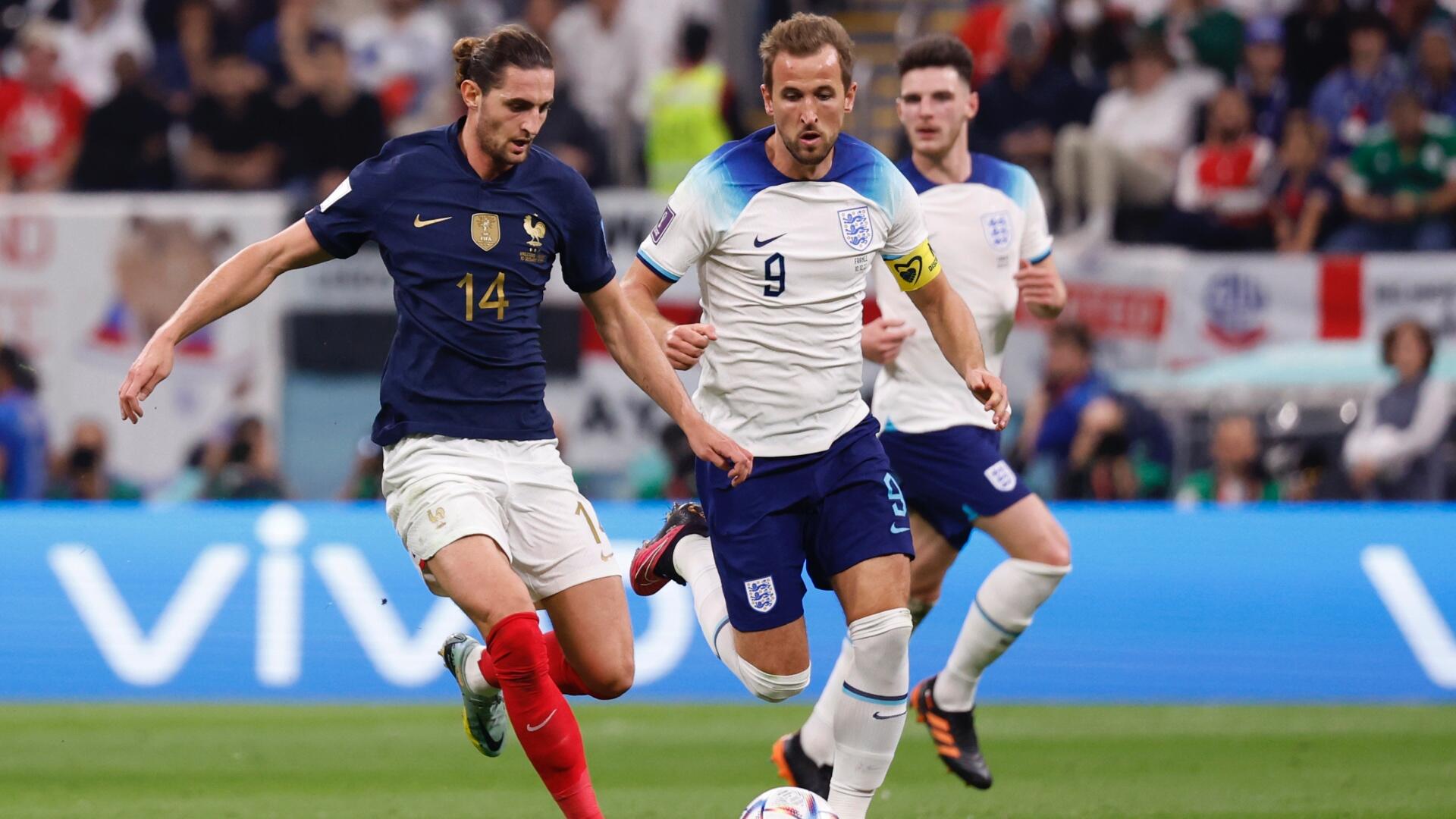 Three England soccer players in white jerseys celebrate, with one wearing a jersey labeled "KANE" and the number 9, set against a blurred stadium crowd.