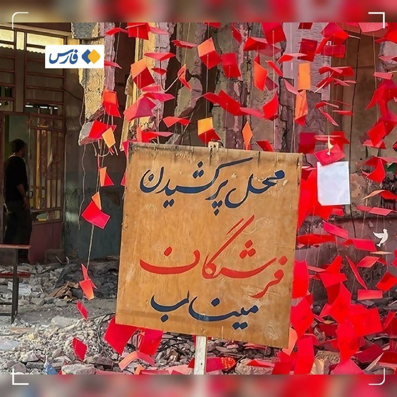 A damaged building interior shows a yellow handwritten Persian sign surrounded by hanging red ribbons, with debris scattered on the floor.