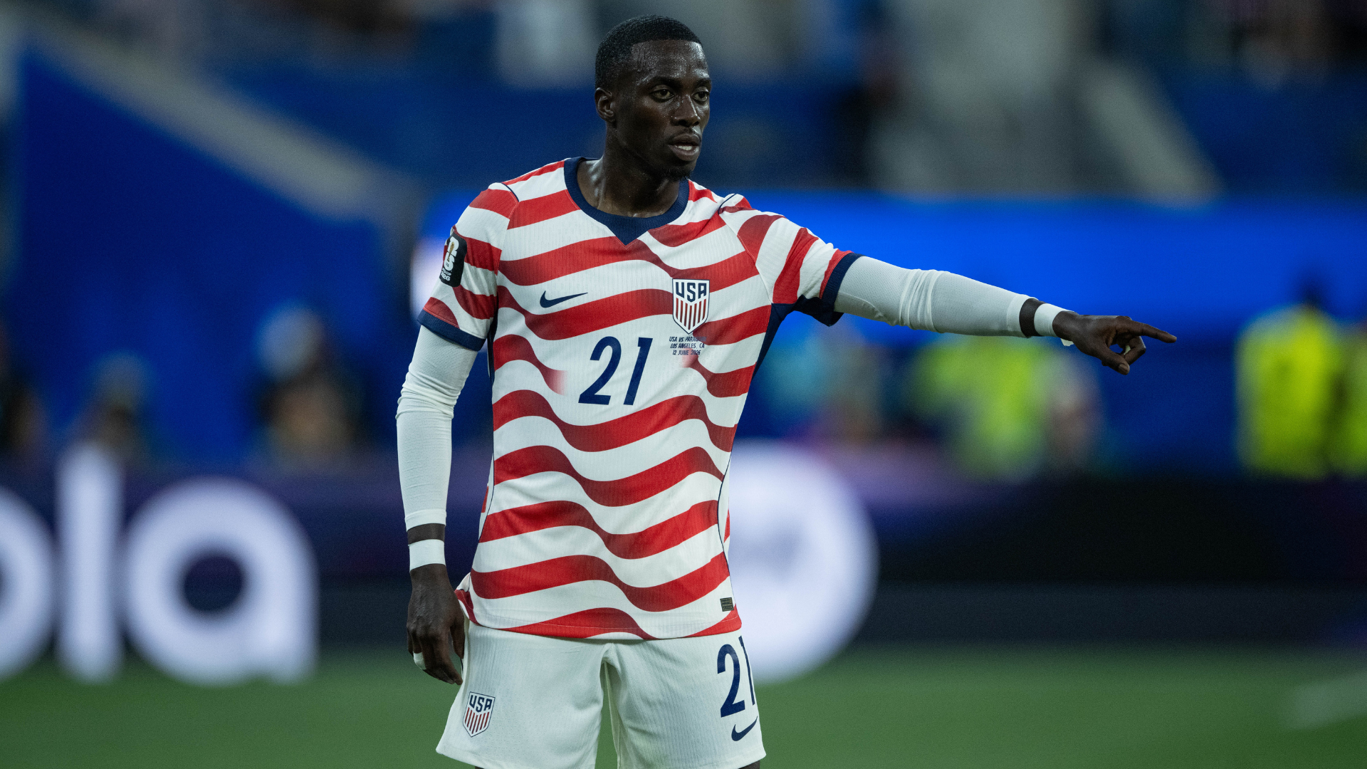 A soccer player in a dark USA jersey with a FIFA World Cup 2026 patch applauds during a match in a stadium.