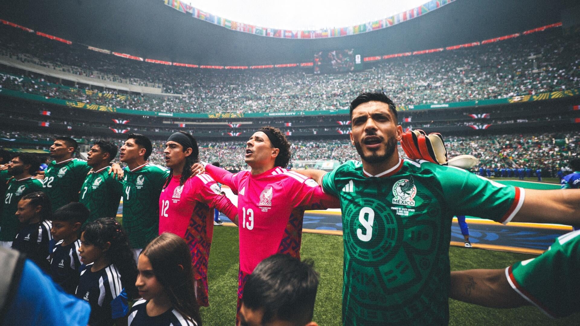 Two soccer players in red Belgium jerseys, numbers 7 (De Bruyne) and 9, raise their joined hands in celebration before a stadium crowd.