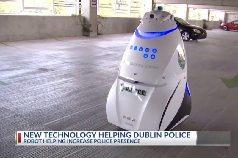 A white police robot with blue lights sits in a parking garage, displayed above a news graphic reading "NEW TECHNOLOGY HELPING DUBLIN POLICE."