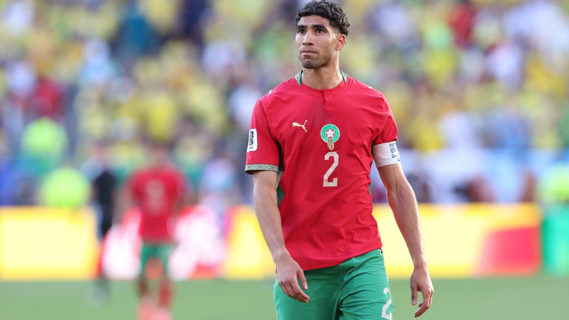 A soccer player wearing a dark blue jersey with the number 10 and a rooster emblem raises both arms in celebration before a packed stadium crowd.