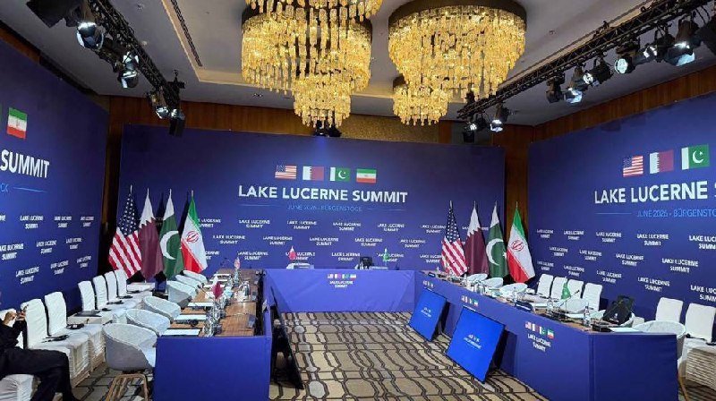 An empty conference room set up for the "Lake Lucerne Summit" in June, featuring U.S., Qatari, Pakistani, and Iranian flags arranged around a central table under ornate chandeliers.