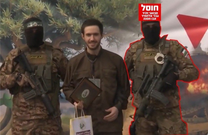 A masked man in a brown jacket holds a framed document and a bag, flanked by two masked, armed figures in military gear against a backdrop showing trees, a flag, and smoke.
