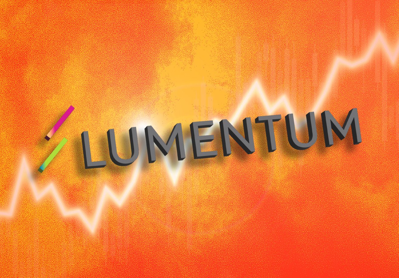 A graphic illustration displays the word "LUMENTUM" in 3D black text over an orange and yellow textured background featuring an upward-trending line chart.