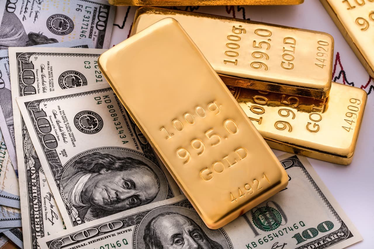 Gold bars stamped "999.9 GOLD" rest atop scattered U.S. $100 bills and a financial chart.