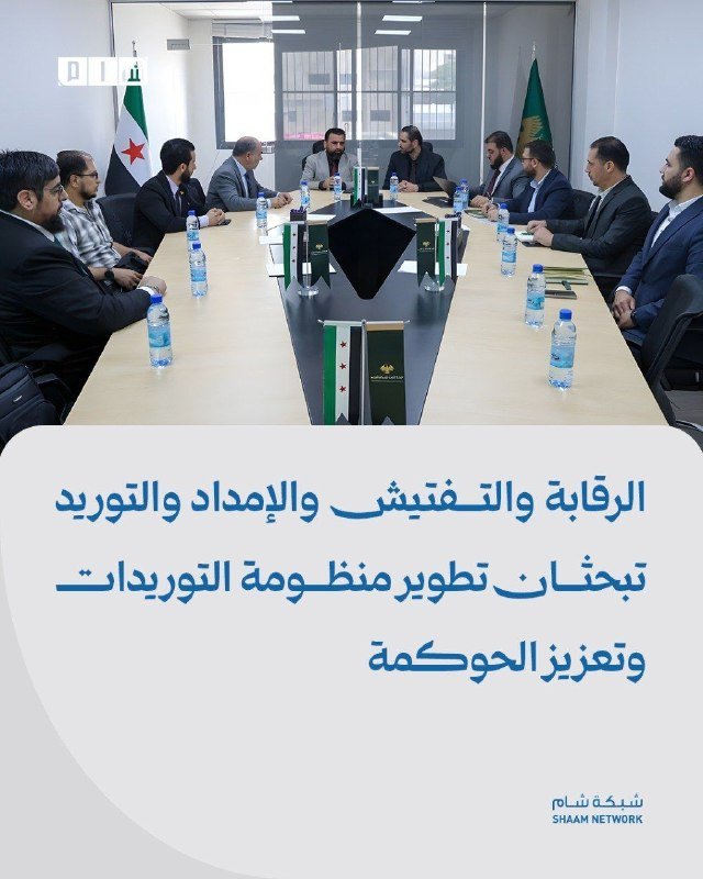 A group of men in suits sit around a conference table displaying opposition flags, with bottled water placed before them and Arabic text overlaid below.