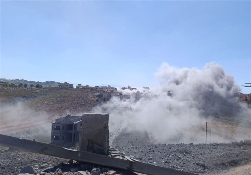 A large dust cloud rises over a rubble-strewn hillside with partially collapsed buildings in the background under a clear blue sky.