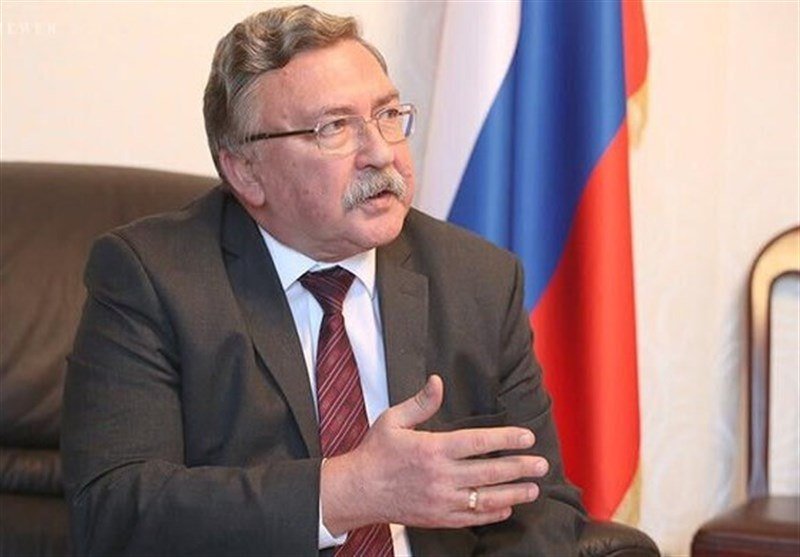 A bespectacled man with a mustache in a dark suit and striped tie gestures while seated, with a Russian flag visible in the background.