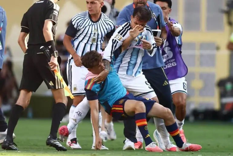 Soccer players in white-and-blue striped jerseys and maroon jerseys clash on a green field while a referee in black stands nearby.