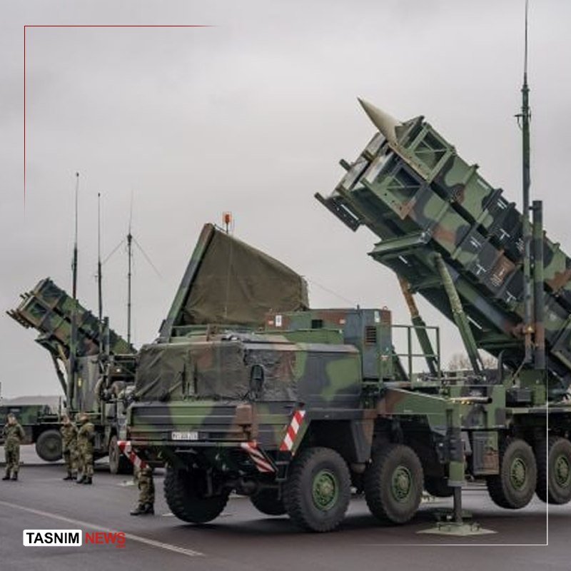 Camouflaged military missile launcher trucks with raised canisters stand on a paved surface as soldiers in uniform stand nearby.