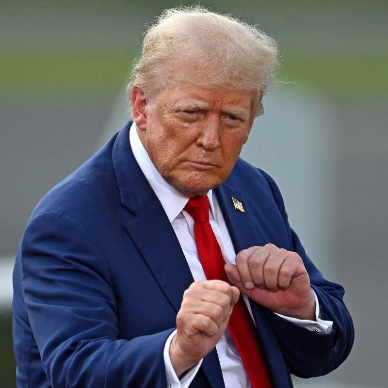 A blond man in a navy suit and red tie speaks passionately at a podium bearing the Presidential seal, gesturing with his hand in front of an audience.