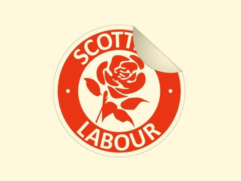 A circular red and white logo featuring a rose design with the text "SCOTTISH LABOUR" appears as a sticker with a curled corner.