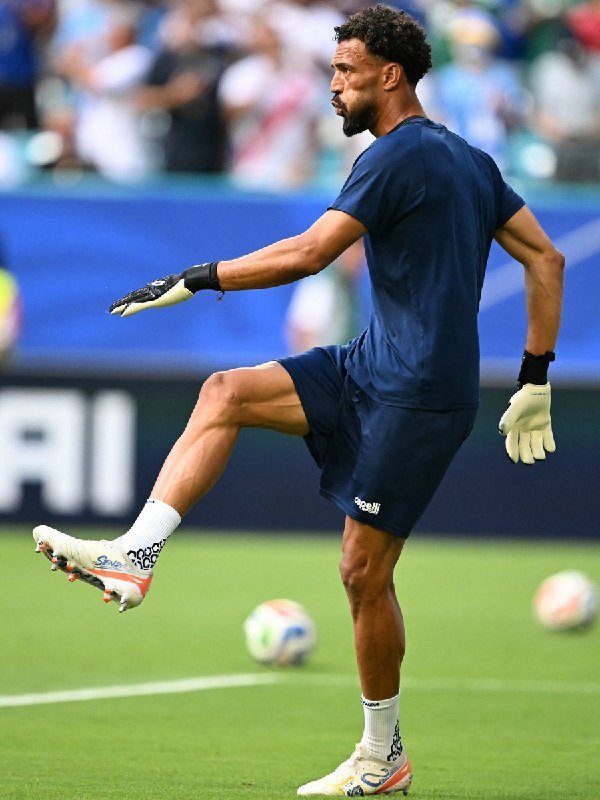 A soccer player wearing a red jersey with the number 10 leaps into the air with clenched fists in celebration, followed by a teammate wearing number 22, inside a packed stadium.