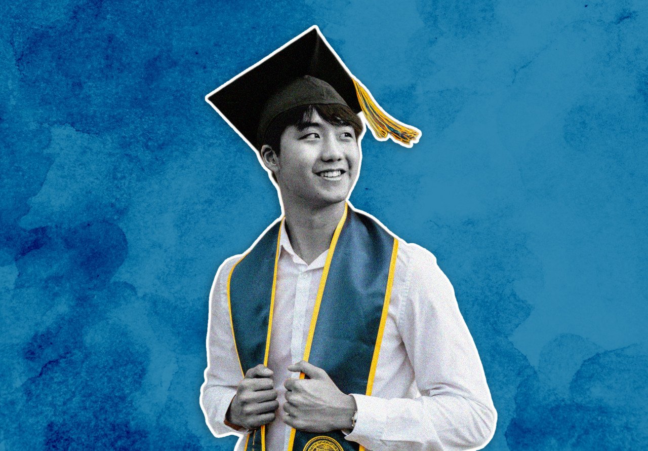 A smiling young man wearing a graduation cap with a yellow tassel and a green and yellow stole over a white shirt, set against a textured blue background.