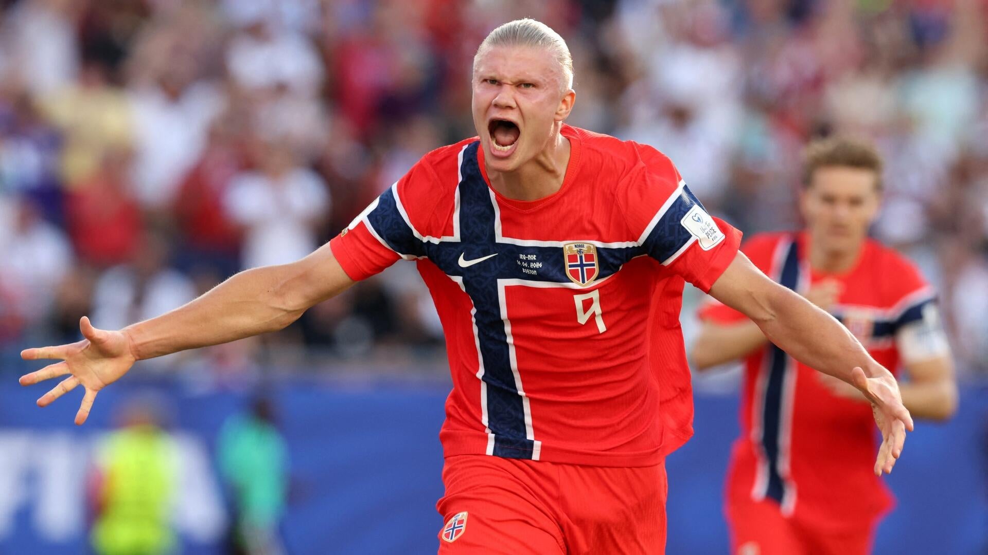 A soccer player wearing a white and navy Bosnia and Herzegovina jersey with the number 11 stands on the field, with a blurred crowd visible in the background.