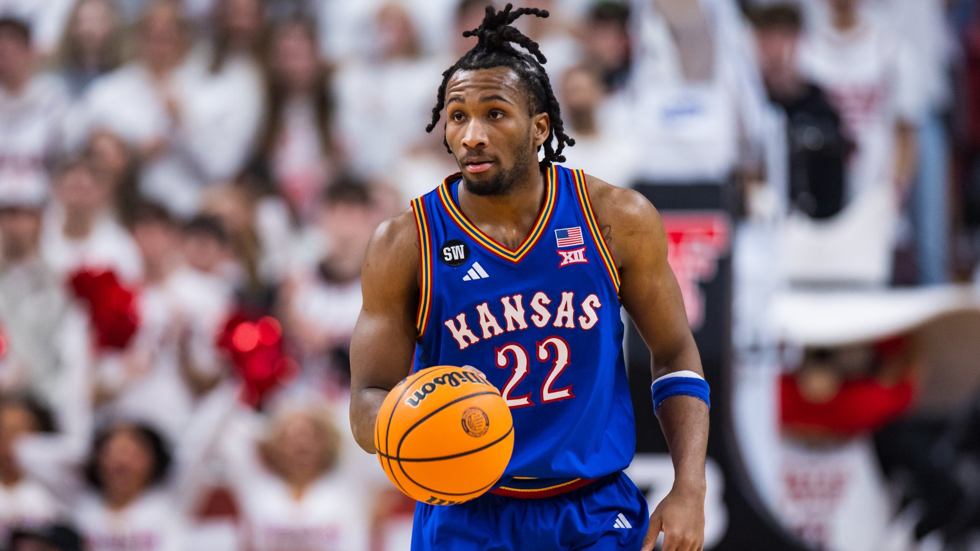 A basketball player wearing a blue Kansas jersey numbered 22 dribbles a Wilson basketball during a game in front of a crowd.