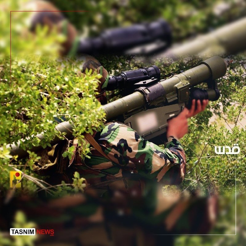 Soldiers in camouflage uniforms aim a shoulder-fired missile launcher through dense green foliage.