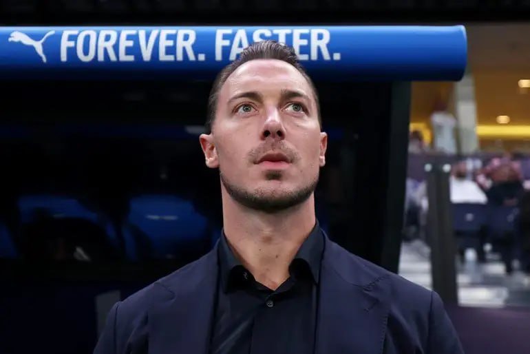 A man in a dark shirt looks upward while standing in front of a blue "PUMA FOREVER. FASTER." sign in what appears to be a stadium setting.
