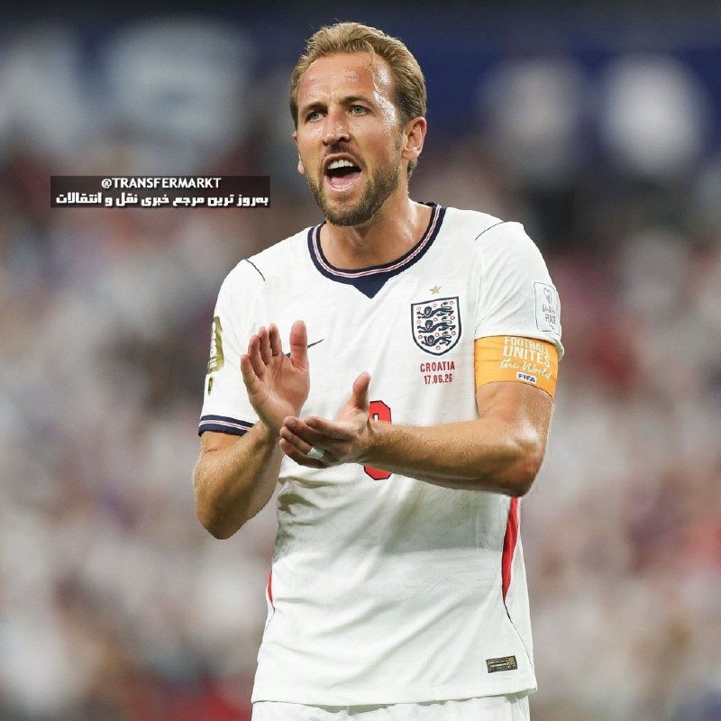 A blonde soccer player in a white England jersey with the "Football Unites the World" captain's armband claps his hands while speaking, set against a blurred stadium crowd.