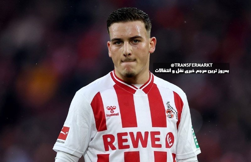 A soccer player in a red-and-white striped Hummel jersey with "REWE" sponsorship stands on the pitch with a blurred stadium crowd in the background.