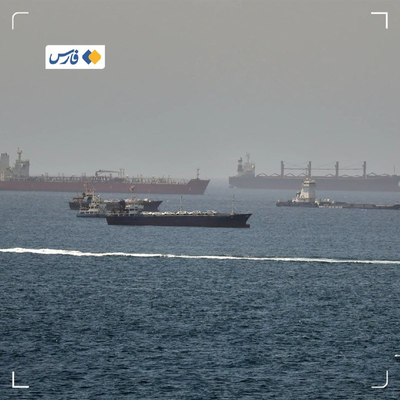 Several large cargo ships and tankers float on hazy gray waters near the horizon.