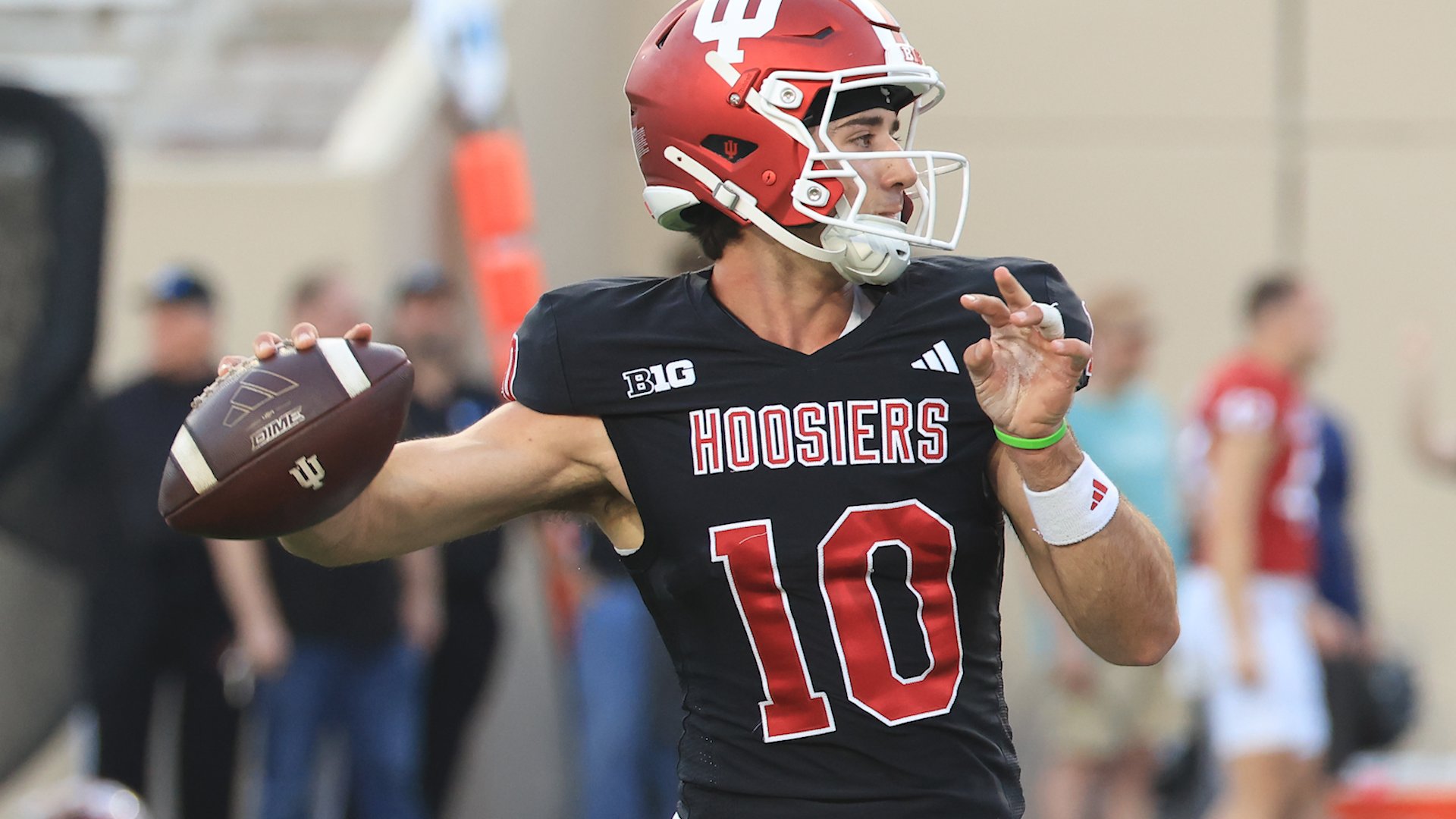 Football players in crimson "Sooners" jerseys link arms with a coach in a black Air Jordan hoodie and red cap on the sidelines.