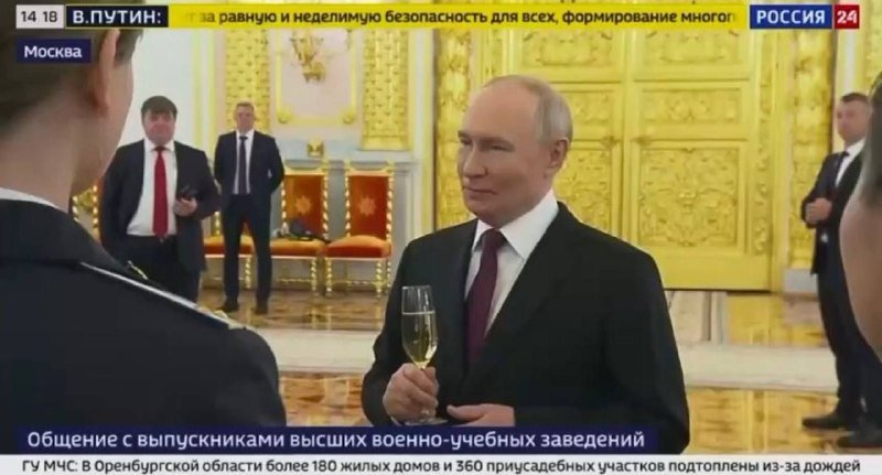 A man in a dark suit holding a champagne flute stands in an ornate gilded hall, with other suited men visible behind him, broadcast by a Russian news channel.