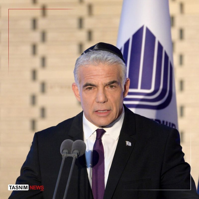 A gray-haired man wearing a dark suit, purple tie, and small skullcap speaks at a podium with two microphones, standing before a flag with a purple emblem.