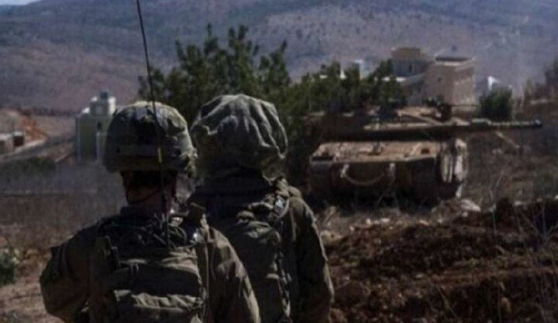 Two helmeted soldiers in camouflage gear stand in a rocky, hilly landscape, with a tank visible in the background.