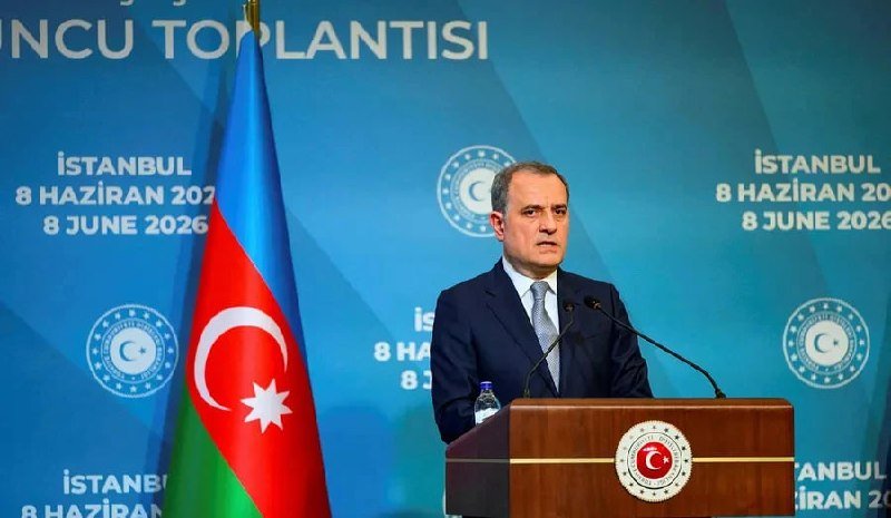 A man in a dark suit speaks at a podium bearing an emblem with "Türkiye," in front of an Azerbaijan flag and a backdrop reading "İstanbul, 8 June 2026."