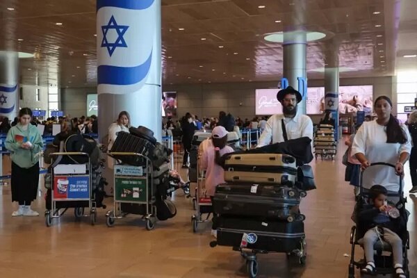 Travelers push loaded luggage carts through an airport terminal featuring large pillars wrapped with Israeli flag designs.
