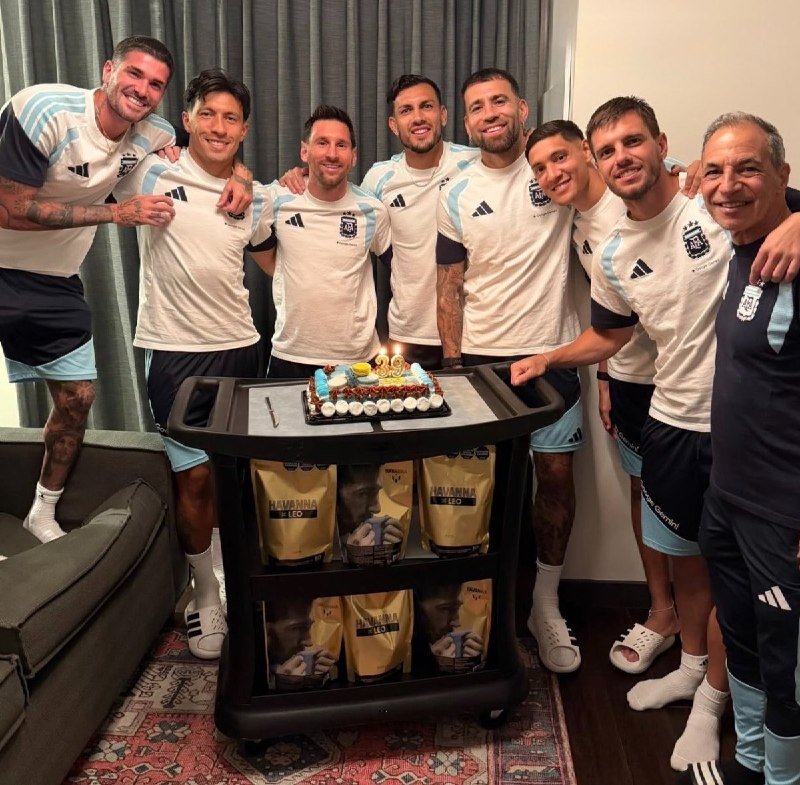 Eight men in matching white and light blue soccer uniforms pose smiling behind a cart holding a lit birthday cake and "Panamma Leo" gift bags.