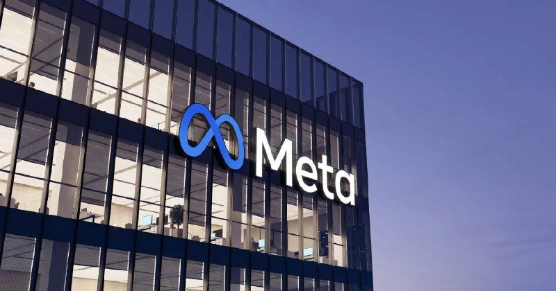 The illuminated "Meta" logo and infinity symbol are displayed on the glass facade of a multi-story office building at dusk.