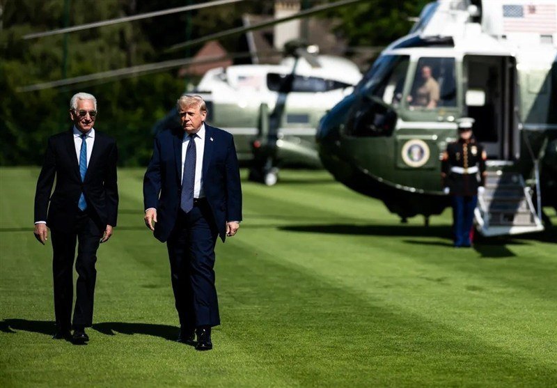 Two men in dark suits walk across a lawn toward the camera, with two green and white helicopters and a uniformed guard visible in the background.