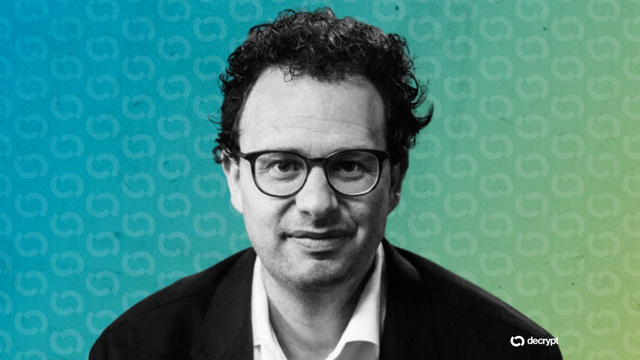 Black-and-white portrait of a curly-haired man wearing glasses and a dark blazer over a white shirt, set against a blue-to-green gradient background with a "decrypt" logo.