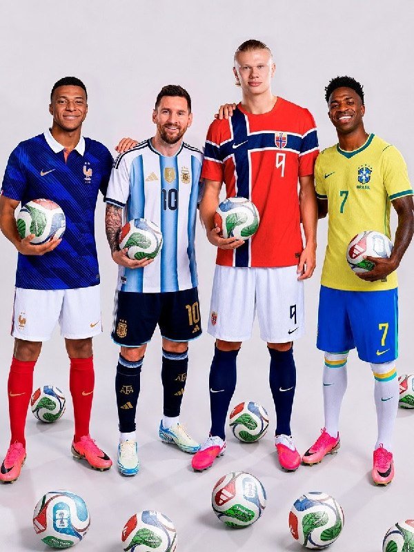 Four soccer players in France, Argentina, Norway, and Brazil national jerseys pose together, each holding a match ball with additional balls scattered at their feet.