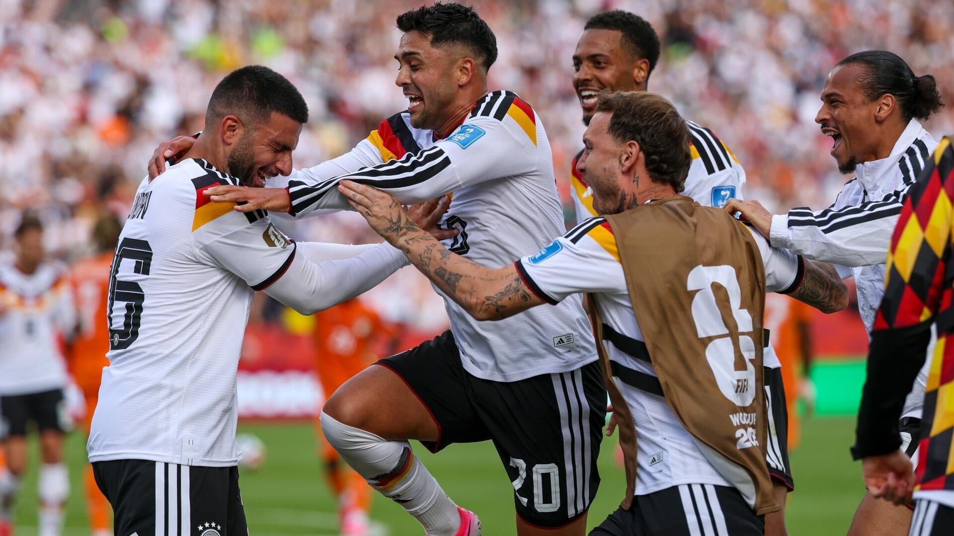Soccer players in white jerseys with black, red, and yellow stripes celebrate together on the pitch in front of a crowded stadium.
