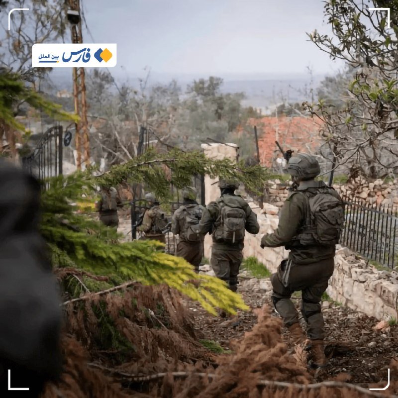Armored soldiers carrying backpacks and rifles walk through a debris-strewn, fenced outdoor area with trees and overcast sky.
