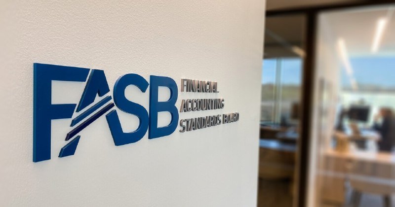 A blue and silver "FASB Financial Accounting Standards Board" logo is mounted on a white office wall beside a glass-walled room.