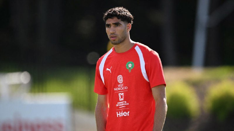 A bearded man in a red Puma soccer jersey with a Morocco crest and "Visit Morocco" branding stands on a field during a training session.