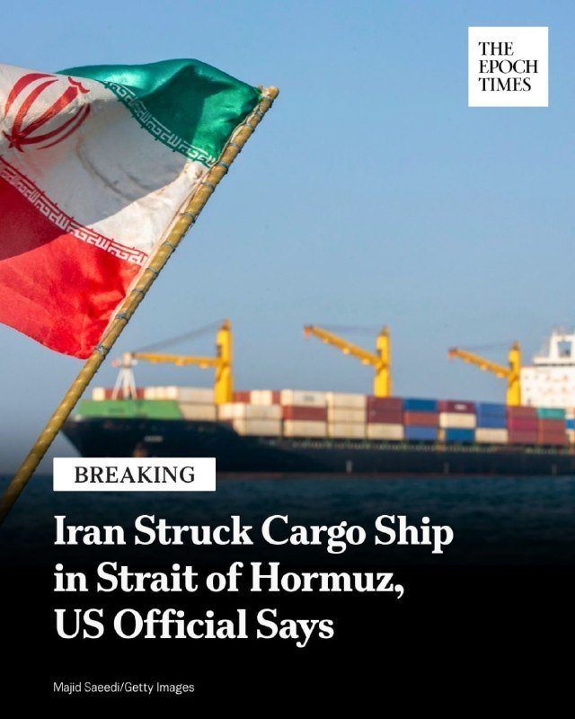 An Iranian flag waves in the foreground before a blurred container ship docked at a port.